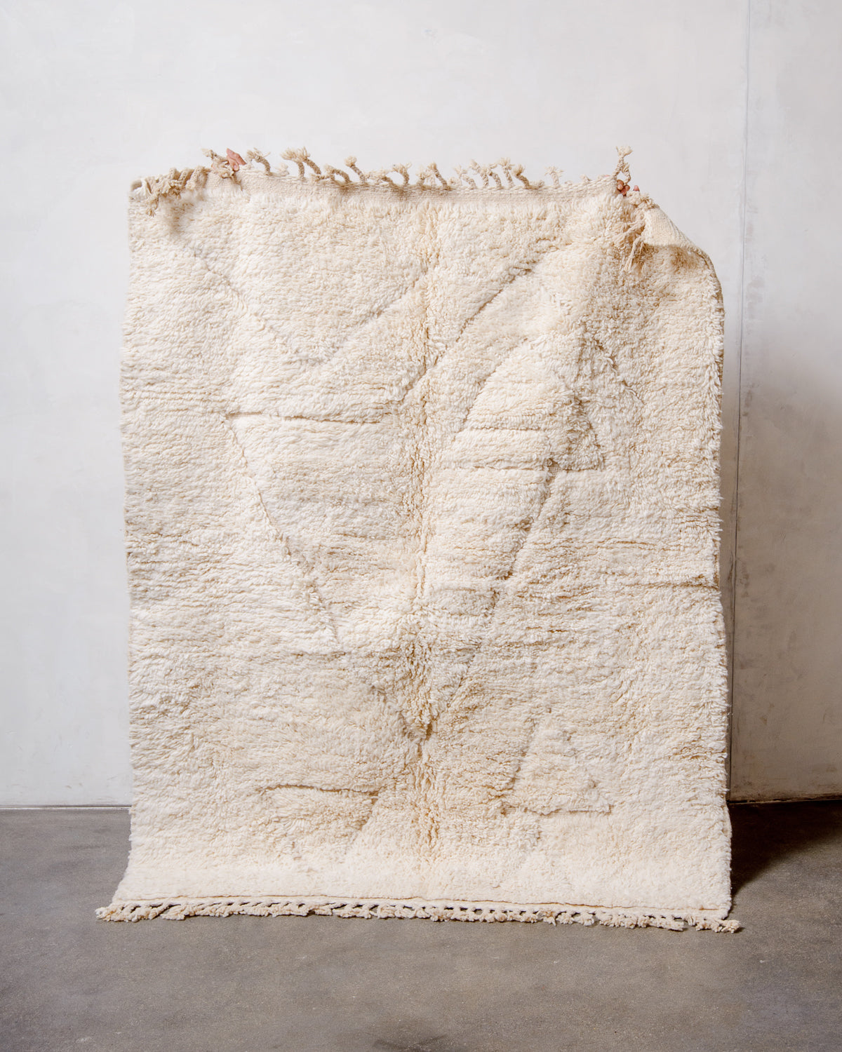 Berberlin Beniourain Rug made of cream wool being held up in front of a white wall.